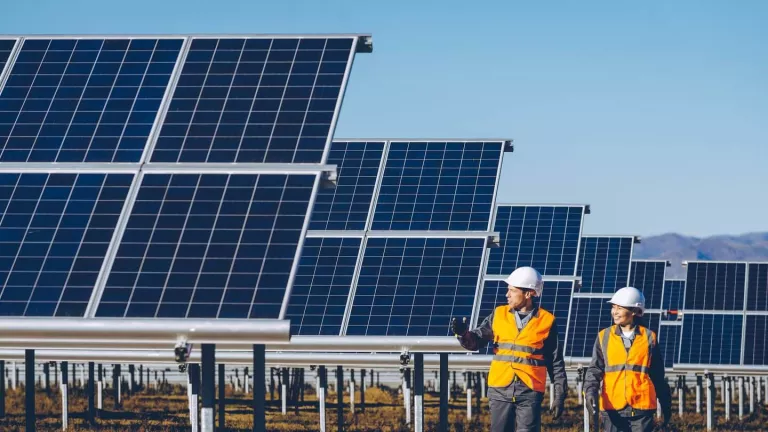 tech - man and woman workers in hard hats walking by solar panels