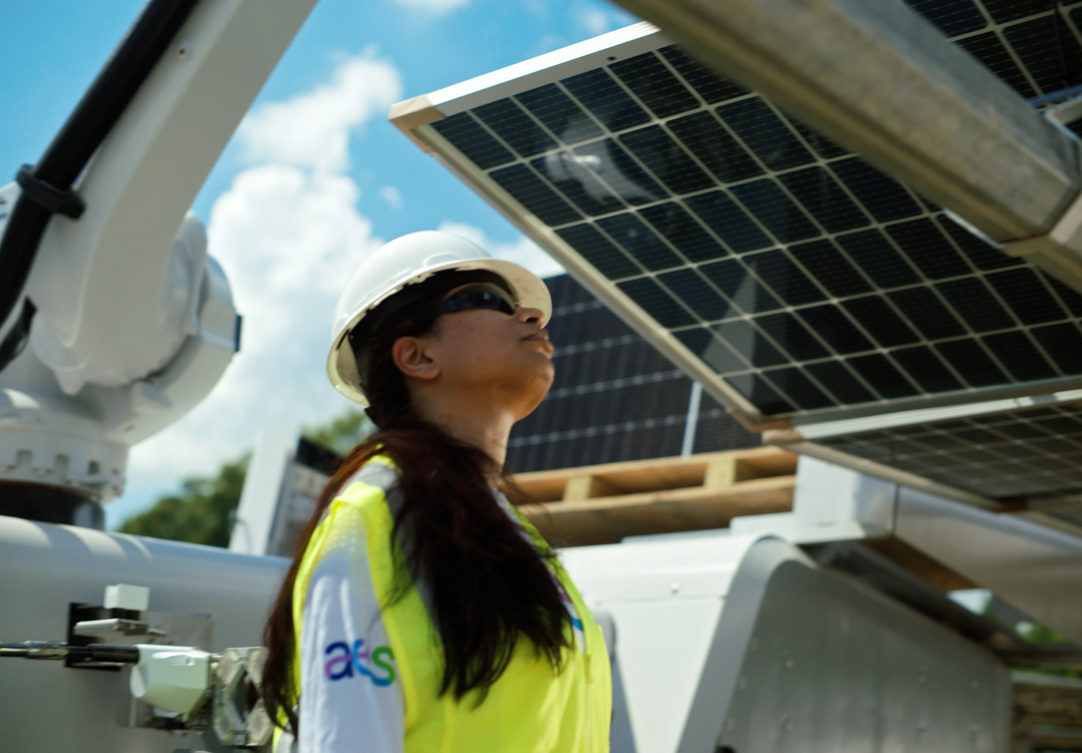 A person wearing a hard hat and safety vest inspects solar panels under a clear blue sky.